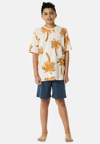 T-shirt crema a maniche corte con stampa di palme arancioni, abbinata a pantaloni corti blu scuro. Il materiale sembra morbido e leggero.