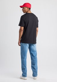 Black cotton t-shirt, fitted design, paired with light blue denim jeans, finished with white sneakers and a red cap.