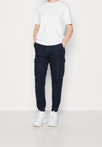 Vit t-shirt med kort ärm i kombination med mörkblå cargo-byxor som har sidofickor och elastiska muddar, kompletterat med vita sneakers.