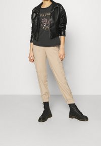 Schwarze Lederjacke, graues Grafik-T-Shirt, beiger tapering Cargo-Hose, schwarze Schnürstiefel, glatte Textur, sichtbare Nähdetails.