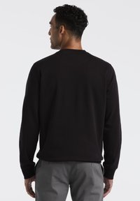 Zwarte long-sleeve shirt gemaakt van zachte stof, met een ronde hals, geribbelde manchetten en een ontspannen fit, gezien vanuit de achterkant.