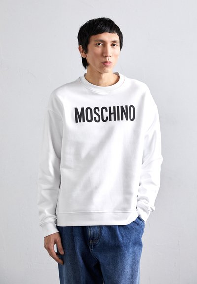 Weißer Sweatshirt mit schwarzem "MOSCHINO"-Logo, Rundhalsausschnitt, weicher Textur, kombiniert mit blauen Jeans. Schlichtes Design mit kräftiger Schrift.