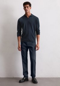 Marineblauwe lange mouwen polo shirt met een kraag, gecombineerd met donkere broeken en zwarte instappers. Gladde stof en een op maat gemaakte pasvorm.