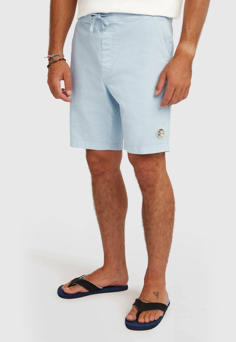 Shorts de bain bleu clair avec une ceinture élastique, un cordon de serrage ajustable, des poches latérales et une petite étiquette logo sur la jambe gauche.