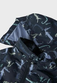 Giacca impermeabile con base blu navy e motivo rettile in azzurro chiaro e verde. Presenta una chiusura con cerniera e un morbido rivestimento interno.