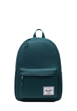 Teal canvas backpack with a rounded shape, front zippered pocket, top handle, and a logo patch on the lower front. Smooth texture.