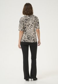 Leopard print top in beige and black, short sleeves, fitted design paired with black flared pants, smooth texture, no visible hardware.