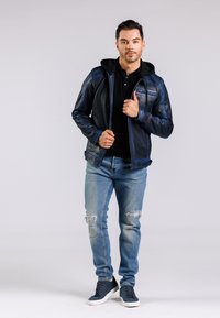 Skórzana kurtka w ciemnoniebieskim kolorze z kapturem, w połączeniu z czarnym polo, jasnoniebieskimi dżinsami z przetarciami i granatowymi sneakersami. Gładka tekstura i dopasowany krój.