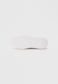 Bijeli potplat tenisice s teksturiranim utorima i dijamantnim uzorkom za bolje prianjanje. Glatka završna obrada s zaobljenom petom i blagim lukom.