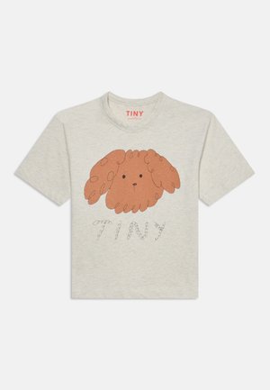 Camiseta beige clara con una sencilla ilustración marrón de la cara rizada de un perro y la palabra "TINY" escrita debajo con letras rizadas.