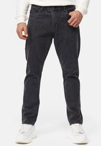 Jeans de mezclilla gris oscuro con un corte relajado, cinco bolsillos, presillas para cinturón y un desgaste sutil. Combinados con zapatillas blancas para un contraste.