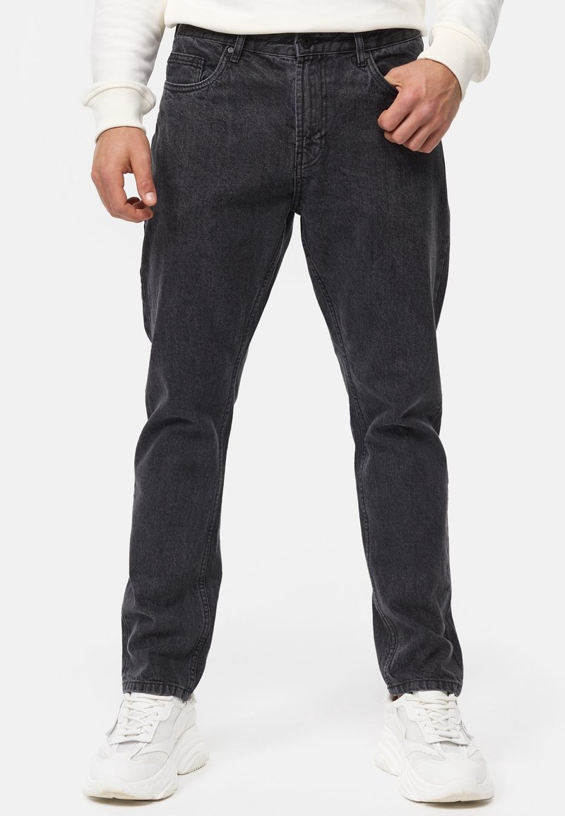 Jeans de mezclilla gris oscuro con un corte relajado, cinco bolsillos, presillas para cinturón y un desgaste sutil. Combinados con zapatillas blancas para un contraste.