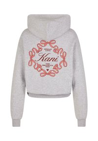 Šedá skrátená mikina s kapucňou vyrobená z mäkkej tkaniny obsahuje centrálne grafické vyobrazenie s červenými mašľami a textom: "Rozširujte lásku Kani BROOKLYNSKÝM SPÔSOBOM."