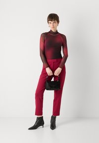 Langsleeve gradient top dat overgaat van donkerrood naar zwart, gecombineerd met strakke rode broek en een kleine zwarte bont handtas. Zwarte enkelboots.
