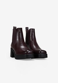 Botas de tobillo de cuero burdeos con una textura suave, paneles laterales elásticos y un tacón grueso negro para estabilidad y comodidad.