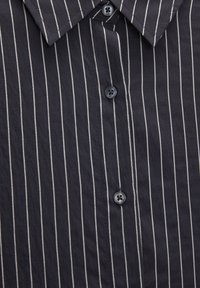 Chemise marine avec des rayures verticales blanches, dotée d'un col boutonné et de boutons sombres, fabriquée en tissu léger avec une texture douce.