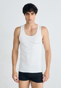 Un débardeur en coton blanc avec un col rond, une coupe ajustée et sans motifs visibles, associé à un short noir. Aucune marque visible.