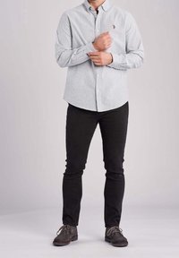 Biała koszula w paski na guziki, czarne dopasowane spodnie oraz szare buty na sznurówki. Charakterystycznym detalem jest małe haftowane godło na koszuli.