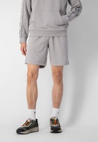 Sweat à capuche gris avec une poche avant et un logo sur les manches, associé à un short gris assorti. Les chaussures présentent des accents multicolores et des semelles texturées.