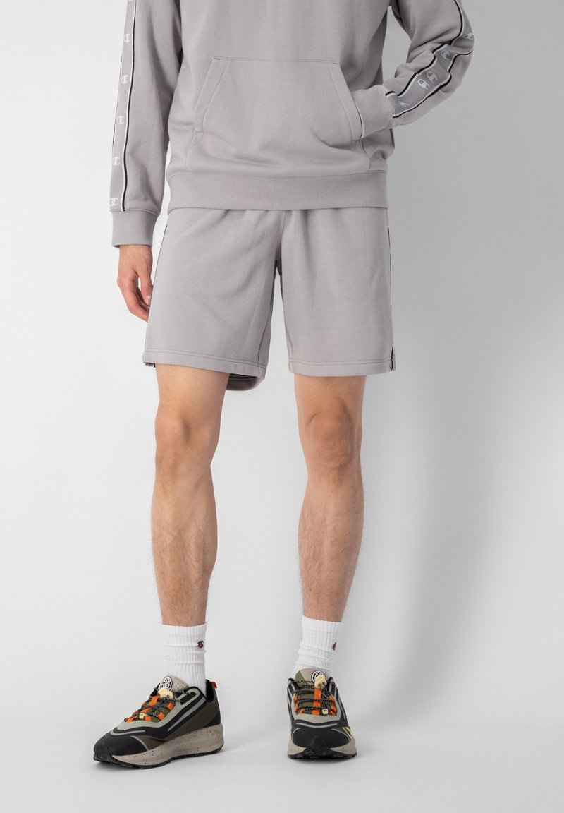 Sweat à capuche gris avec une poche avant et un logo sur les manches, associé à un short gris assorti. Les chaussures présentent des accents multicolores et des semelles texturées.