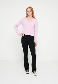 Ροζ ελαφρύ πουλόβερ με μακριά μανίκια και V-λαιμόκοψη, σε συνδυασμό με μαύρο παντελόνι καμπάνα και μαύρα αθλητικά παπούτσια· απλός σχεδιασμός με άνετη εφαρμογή.