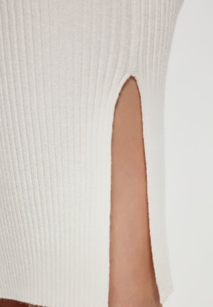 Witte geribde top met een zijsplit, voorzien van een zachte textuur en een aansluitend ontwerp. Opmerkelijke details zijn een nette zoom en verticale ribbels.