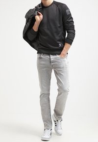 Sudadera negra con mangas raglán, jeans grises y zapatillas blancas. Los detalles notables incluyen un logo en la sudadera y una textura suave.