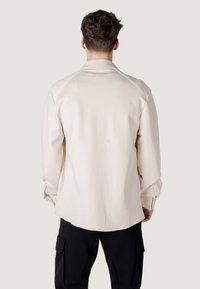 Lichtbeige lange mouwen shirt met een ronde zoom en knopenmanchetten. Glad textuur en raglan mouwen. Effen kleur, minimale details.