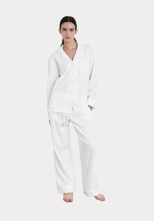Witte katoenen pyjama set bestaande uit een shirt met knopen en een zak, en loszittende broek met een elastische tailleband en trekkoord.