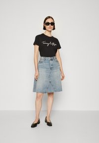 Svart bomull T-skjorte med hvit skriftlogo, sammen med en lyseblå denim A-linje skjørt med frynset hem og skrå sømmer. Svarte sko.