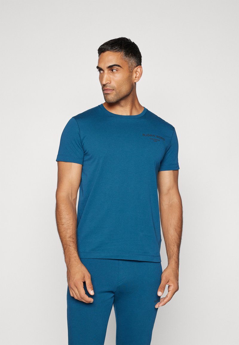 Krátký rukáv, klasický střih trička v tmavě modré barvě z bavlny se slim fit, s malým černým potiskem loga na levé části hrudi.