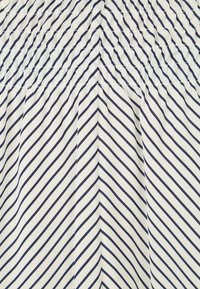 Tissu blanc avec des rayures diagonales bleu marine ; présente un élastique froncé en haut et une texture lisse et fluide tout au long.