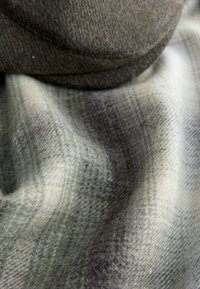 Woolen fabric featuring a checkered pattern in muted shades of gray and cream, draped with a dark brown textured cap positioned above.