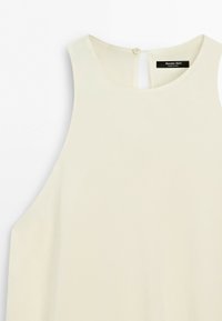 Haut sans manches couleur crème avec un col rond et une petite fermeture par bouton dans le dos, montrant l’étiquette de la marque Massimo Dutti.