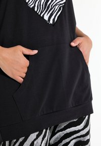 Top nero con un design a forma di cuore a stampa zebra, dotato di una tasca frontale e una texture liscia, abbinato a pantaloni a righe zebra in bianco e nero.