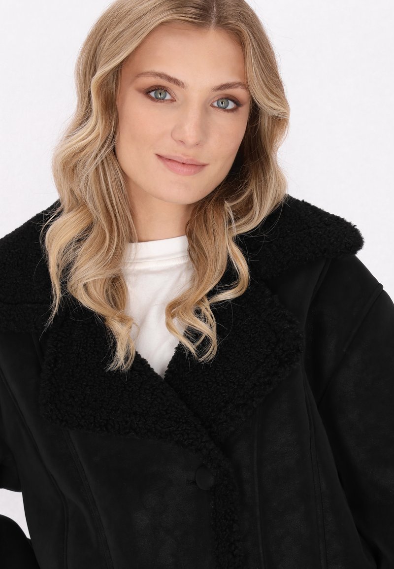 Veste en fausse fourrure noire avec un grand col, un tissu texturé et une fermeture à bouton, conçue avec une coupe décontractée et une finition lisse.