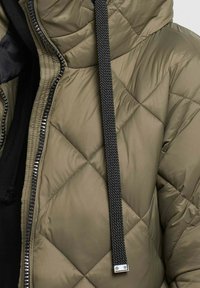 Olive green quilted jacket with a black textured drawstring, silver zipper, and side pockets. Smooth, padded material with diamond pattern.