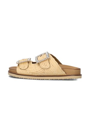 Beige woven slide sandal featuring two adjustable straps with decorative rhinestone buckles and a flat rubber sole.