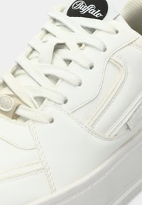 Λευκό αθλητικό παπούτσι κατασκευασμένο από ομαλό συνθετικό υλικό με επίπεδα κορδόνια, ετικέτα λογότυπου στη γλώσσα και παχιά, υφασμένη σόλα. Διακριτικές ραφές.