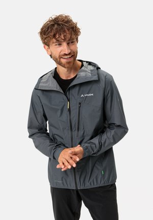 Giacca leggera grigia con cappuccio, cerniera frontale e due tasche con cerniera. Presenta dettagli a contrasto e un accento verde vicino all'orlo.