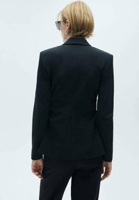 Czarna, dopasowana marynarka o eleganckim kroju, z klapami oraz gładką fakturą. Widok z tyłu ukazujący długie rękawy i minimalne szwy.