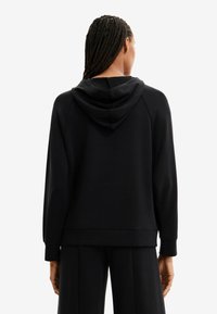 Felpa nera con cappuccio caratterizzata da una texture morbida e opaca, grande cappuccio e spalle scese. Le maniche e l'orlo a coste offrono una vestibilità rilassata.