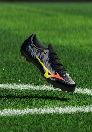 Czarny but piłkarski z żółto-pomarańczowym logo unoszący się nad zielonym boiskiem z białymi oznaczeniami linii.