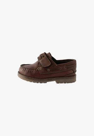 Scarpa da barca in pelle marrone con punta arrotondata, dettagli di cucitura e suola imbottita; presenta una cinghia in velcro e lacci sui lati.