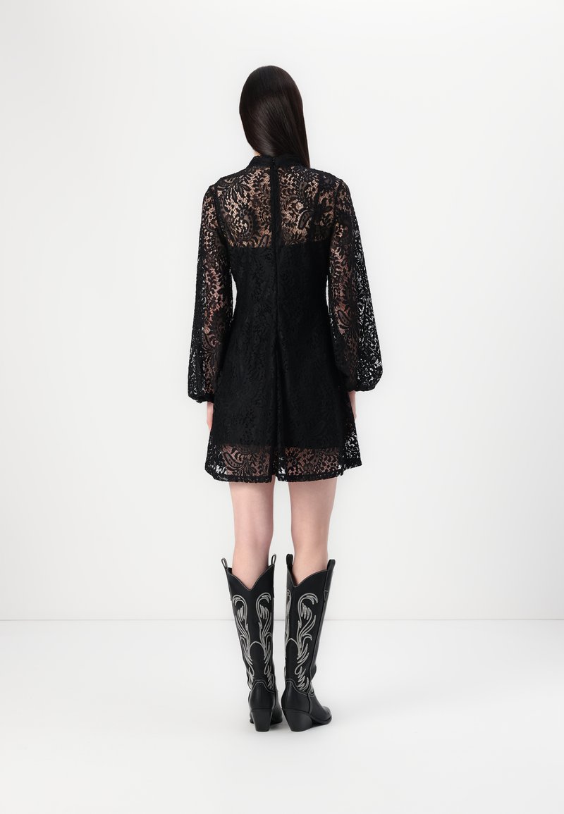 Schwarzes Spitzenkleid mit filigranen Blumenmustern, langen Puffärmeln und ausgestelltem Schnitt, kombiniert mit knielangen schwarzen Cowboy-Stiefeln.