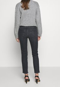 Jeans ajustados de lavado oscuro con dobladillos desgastados, acompañados de un suéter de punto gris claro. Detalles de bolsillos traseros visibles y tejido texturizado del suéter.