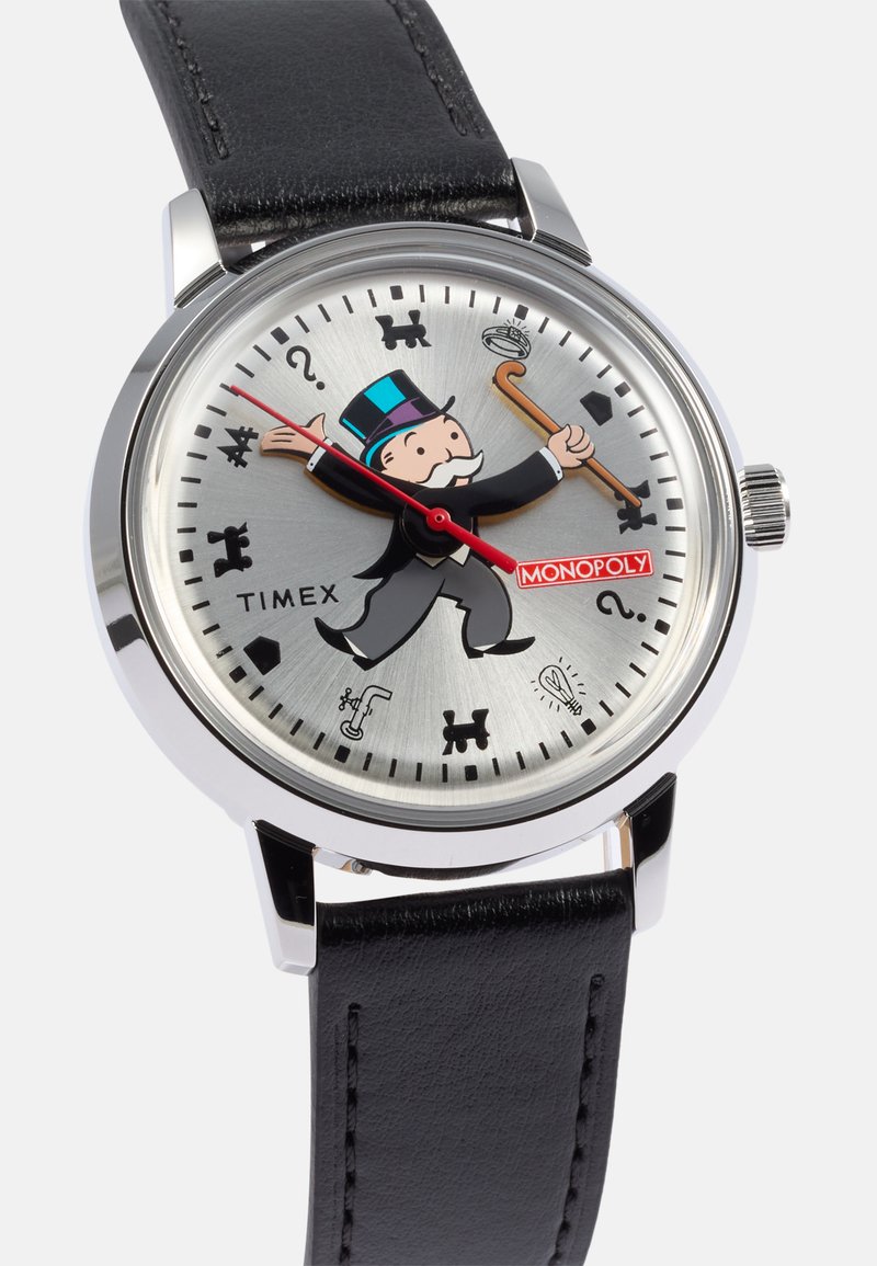 Reloj Timex Monopoly que presenta una esfera plateada, correa de cuero negro e ilustración de un personaje de Monopoly, con manecillas e íconos rojos.
