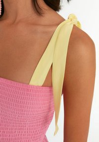 Rosa geraffte Kleid mit einem gelben Bändchen, das an der Schulter gebunden ist, ausgestattet mit einer strukturierten Oberfläche und einer Nahaufnahme des oberen Rückens.