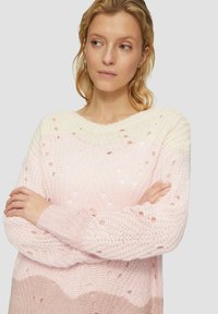 Pull en tricot léger avec un dégradé allant du blanc au rose doux. Présente des détails ajourés et des poignets côtelés. Encolure ronde, coupe décontractée.
