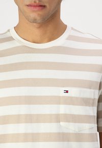 Beige and white striped short-sleeve t-shirt made of soft material. Features a chest pocket with a small logo. Crew neck design.